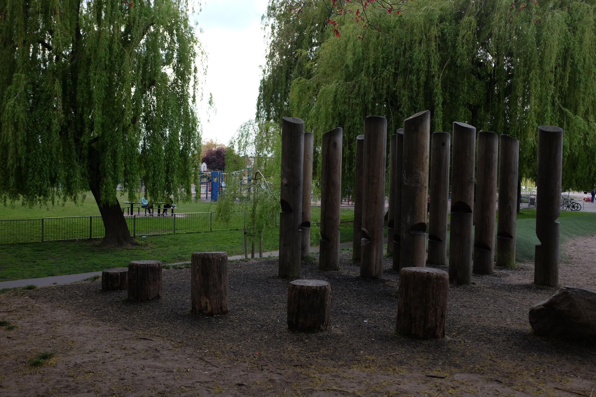 image shows playground in background, trees and wooden pillar play-features in foreground